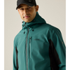 A man wearing a teal and black hooded jacket and a black baseball cap, photographed against a plain light beige studio background.