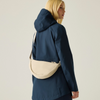 a woman standing wearing a navy rainjacket with a cream bag strap over her shoulder