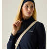 A blonde model wearing a navy blue quarter-zip pullover with a white embroidered logo on the chest, a matching navy beanie, and a beige crossbody bag strap against a plain light beige background.
