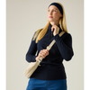 A woman wearing a navy mock-neck athletic top, blue pants, and a navy headband, carrying a cream-colored shoulder bag against a plain light beige studio background.