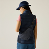 A woman wearing a navy quilted puffer vest, blue cap, and pink t-shirt is shown from the back, wearing a dark navy crossbody bag with a zippered pouch on her back.
