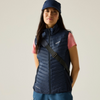 a woman wearing a nacy gilet with a pink tshirt underneath and a navy had and navy shorts on beige background
