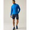 A man wearing a bright blue long-sleeve quarter-zip athletic pullover, navy running shorts, and blue running shoes, standing against a plain light gray studio background.