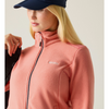 A woman wearing a coral pink fleece zip-up jacket and a navy blue baseball cap, shown in a close-up profile against a light beige background.