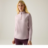 A woman modeling a light pink quarter-zip long-sleeve athletic top with a small tonal logo on the left chest, paired with dark purple leggings, against a plain light gray studio background.