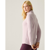 A blonde woman wearing a light pink long-sleeve mock neck athletic top and dark purple leggings, shown from a side-back angle against a light gray studio background.