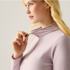 A close-up of a blonde woman wearing a light pink mock-neck long-sleeve top, pulling the zipper tab to show the front closure.