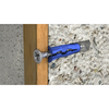 A blue and gray wall anchor screw installed between a wooden trim board and a textured concrete wall.
