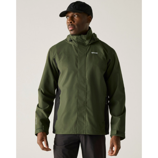 A man wearing an olive green hooded rain jacket with black side panels, a black cap, and dark pants, photographed against a plain light gray studio background.